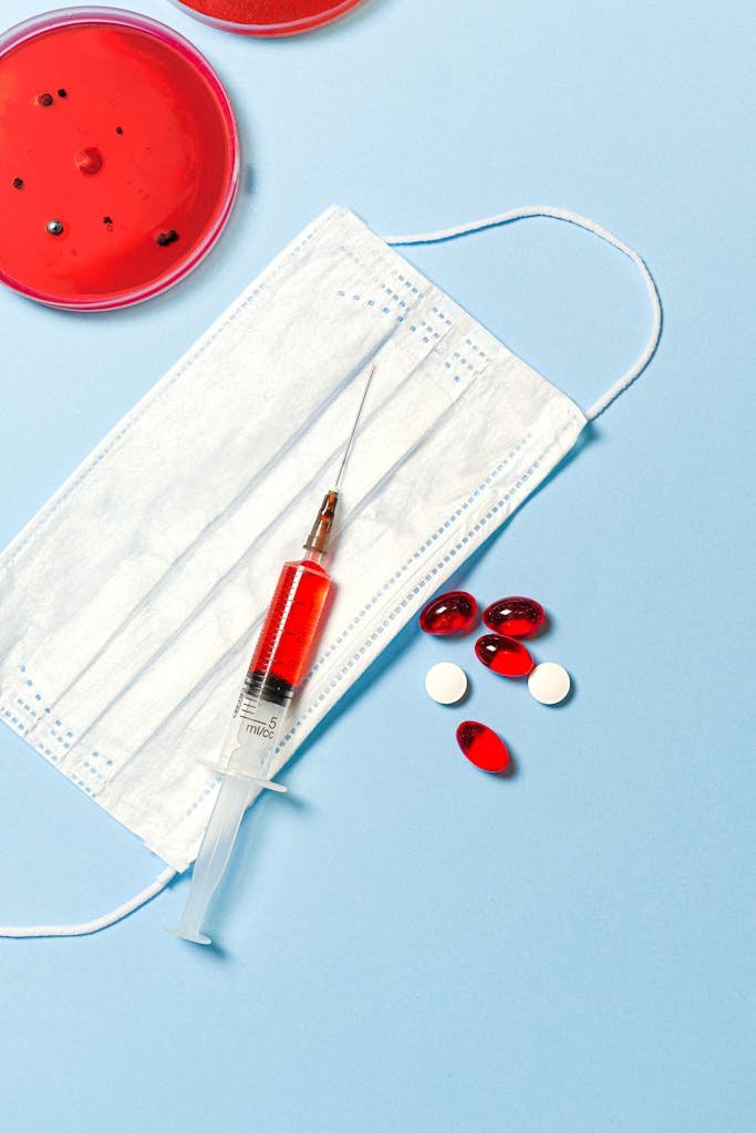 photo by anna shvets Face mask, syringe, and pills on a blue background, symbolizing healthcare and medical research.